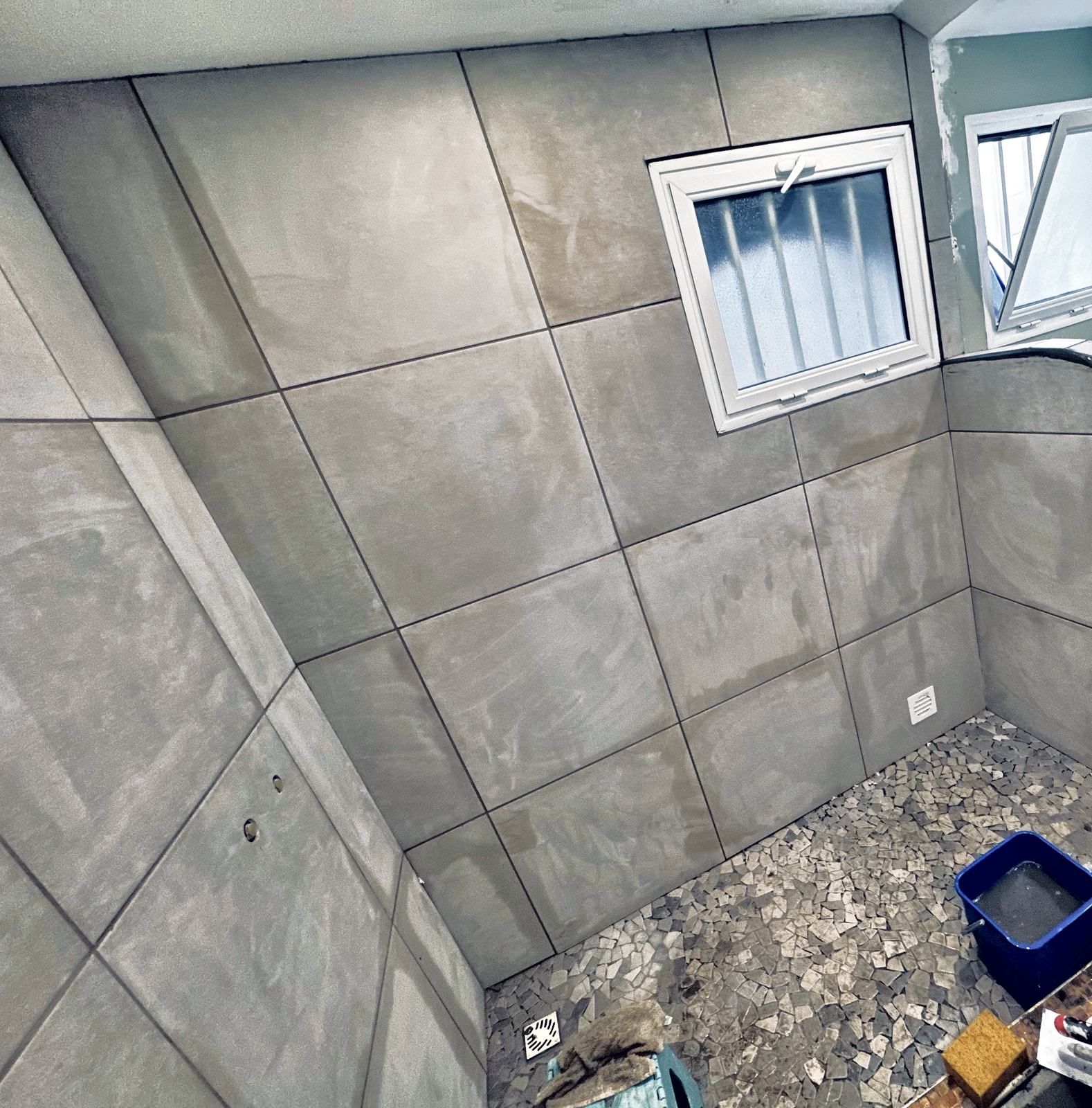 Douche en cours de finition : carrelage grand format et sol en galets