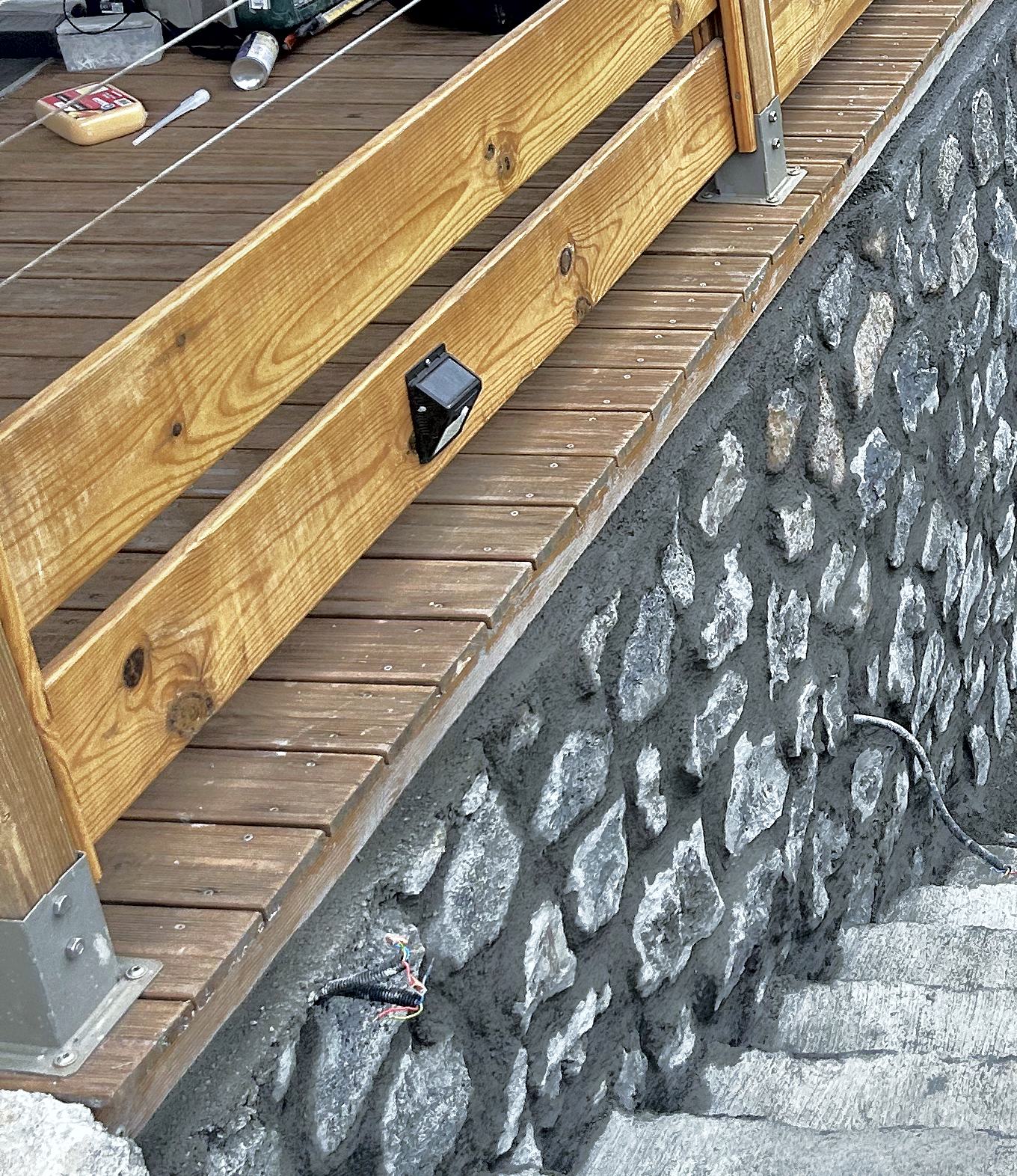 Terrasse en bois avec garde-corps sur un soubassement en pierre de basalte