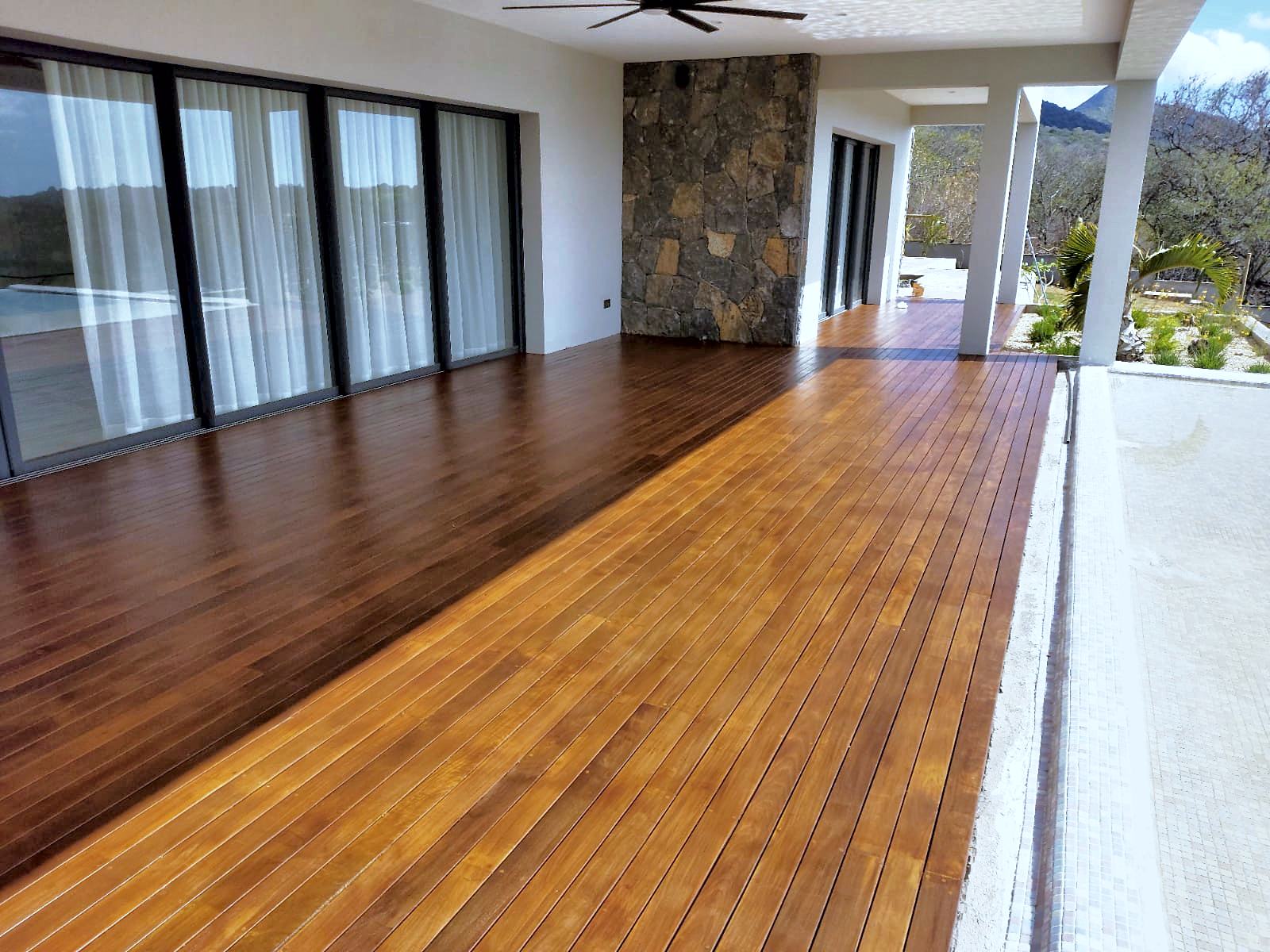 Terrasse en bois exotique rénovée et saturée, sous la varangue d'une villa, mur en pierre